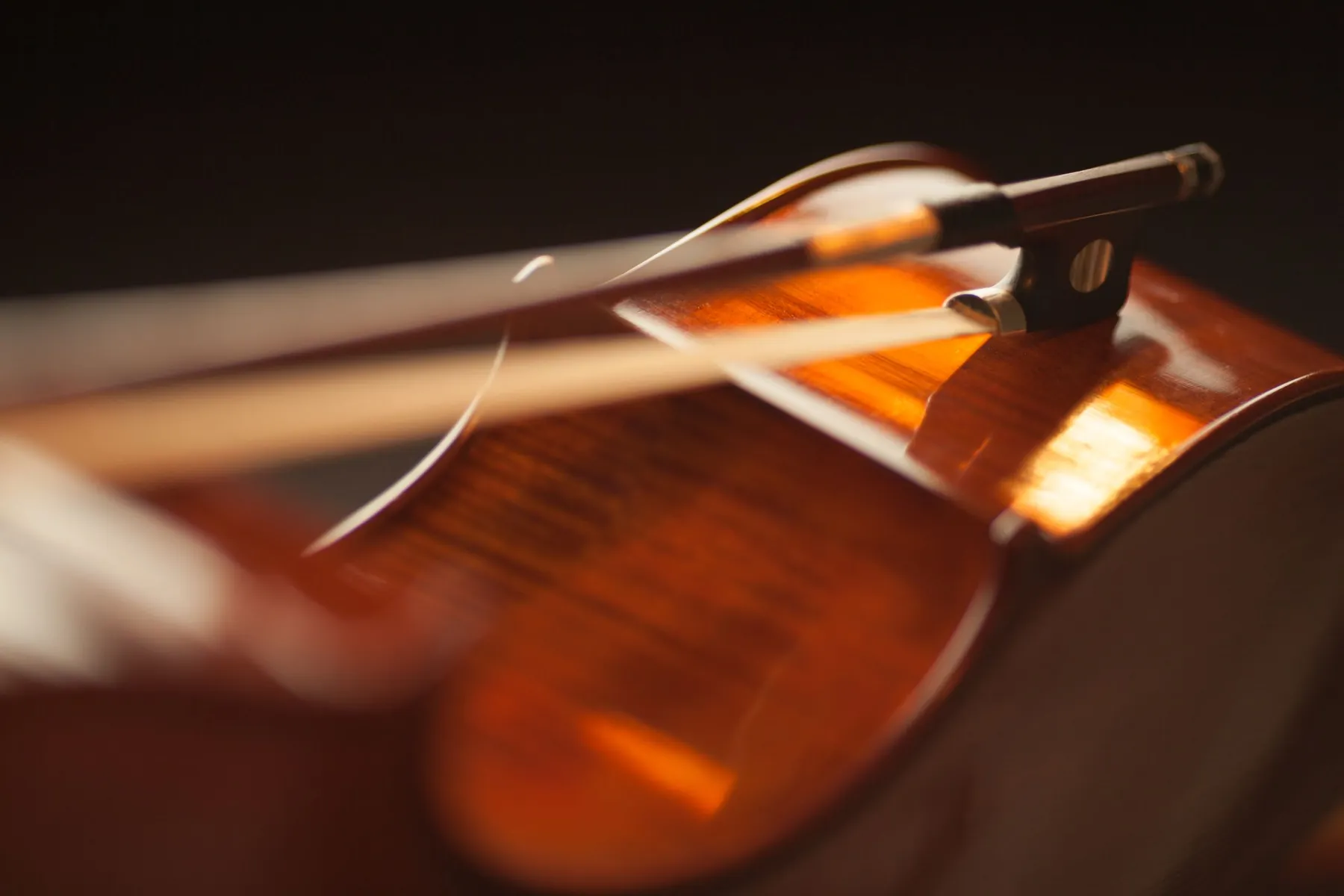 A violin bow resting across the body of a violin in warm light