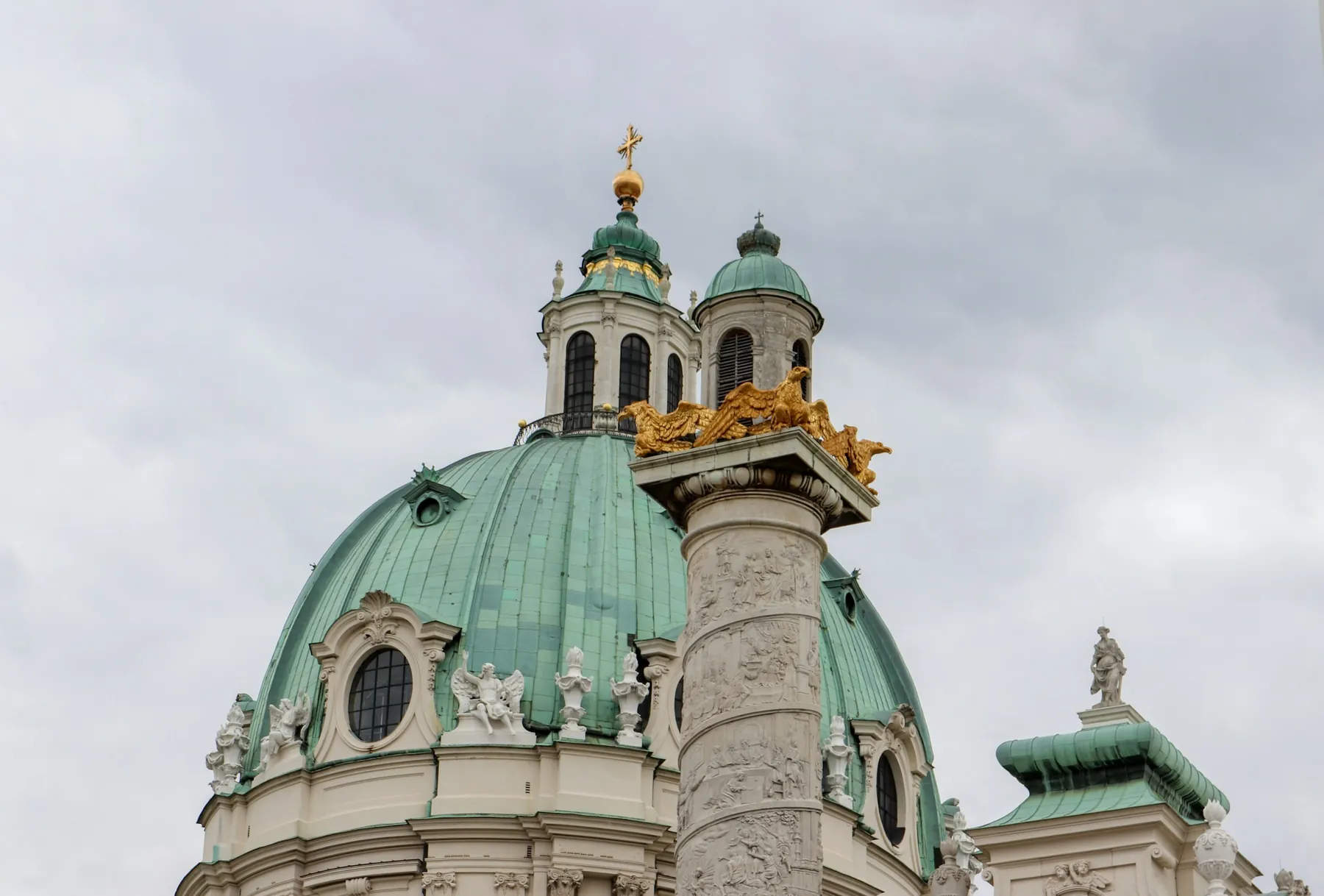 The green copper dome of Karlskirche with its gilded lantern, and one of the two relief-wrapped columns beside it