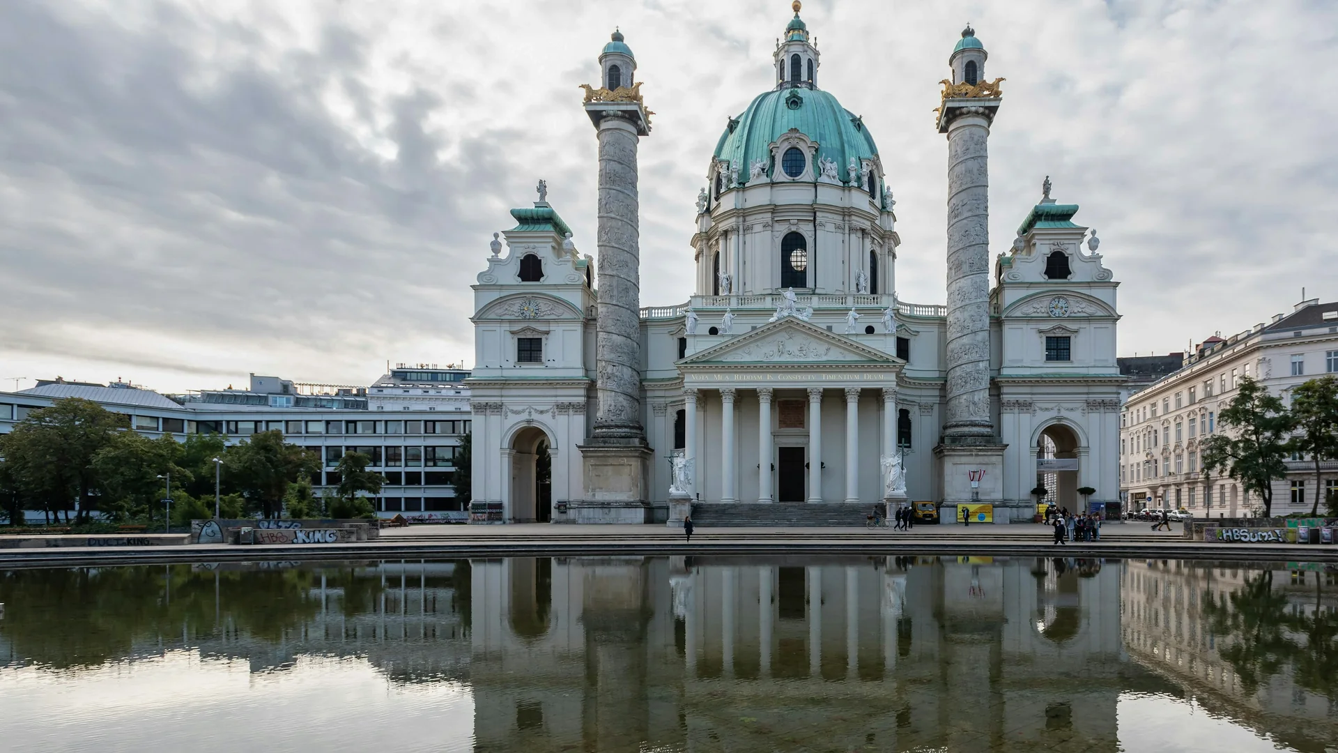 Karlskirche and its two relief-wrapped columns across the reflecting pool on Karlsplatz under a soft grey sky